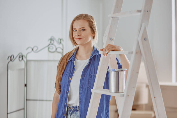 Beautiful young woman on a white wooden stepladder. Ready to repair the room. Women housework concept - Zdjęcie, obraz