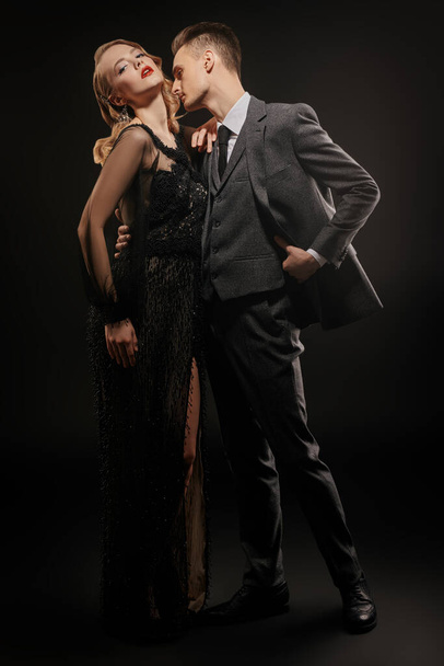 Beautiful passionate couple of man and woman in expensive evening dresses on a black background. Couple in love. Beauty, fashion.  Studio portrait. Full length - Fotoğraf, Görsel