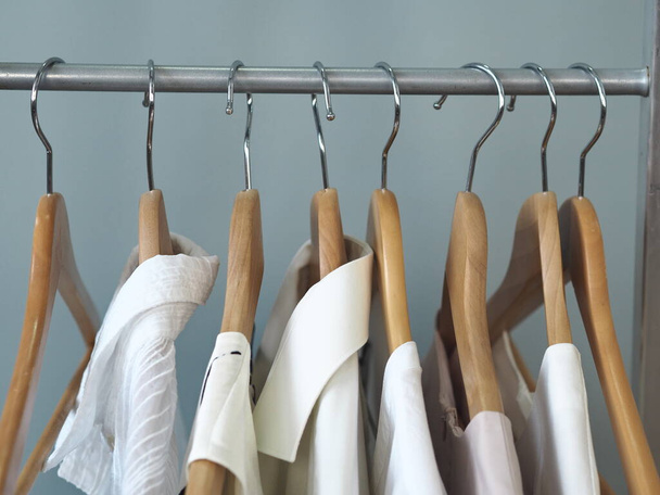 Storage things white and bright clothing on the shoulders of the hangers. Products made of natural fabrics on a gray background. - Photo, Image