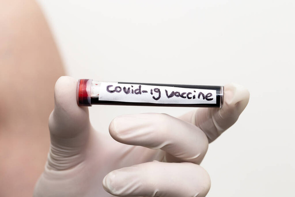 Vacuna Covid-19 en tubo sanguíneo, médico con guantes médicos sosteniendo un tubo sanguíneo con Coronavirus positivo 2019-nCoV Blood Sample with injection
. - Foto, imagen