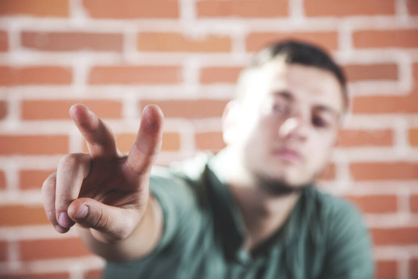 молодий бізнесмен два пальця на фоні цегляної стіни
 - Фото, зображення