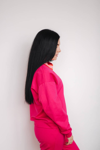 Viehättävä nuori malli vaaleanpunaisissa verkkareissa. Nainen esittelee vaatteita studiossa. Valkoinen tausta
 - Valokuva, kuva