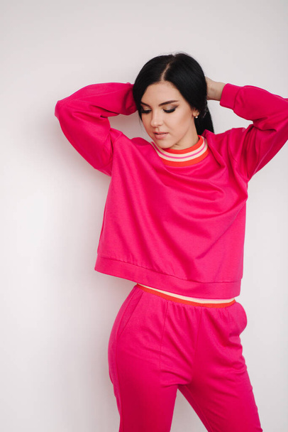 Attractive young model in pink tracksuit. Woman demonstrating clothes in studio. White background - Foto, imagen