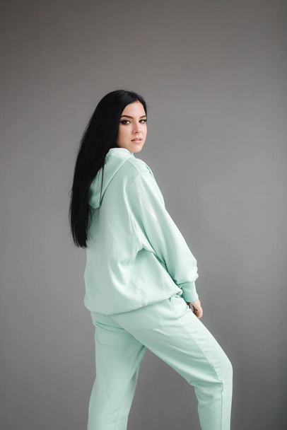 Attractive young model in tracksuit. Woman demonstrating clothes in studio. Gray background - Photo, Image