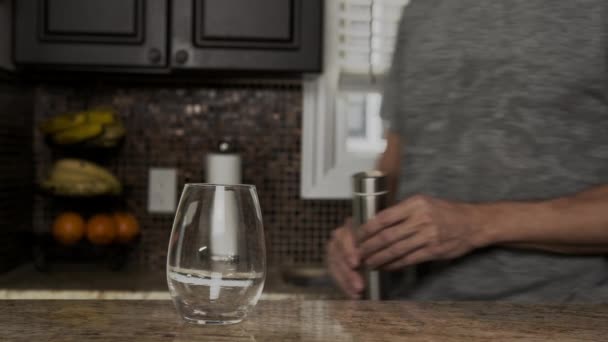 Young man in a gray T-shirt pours water into a glass from a thermos or plastic bottle in a beautiful fashionable kitchen. healthy lifestyle. Handsome man is thirsty. - Materiaali, video