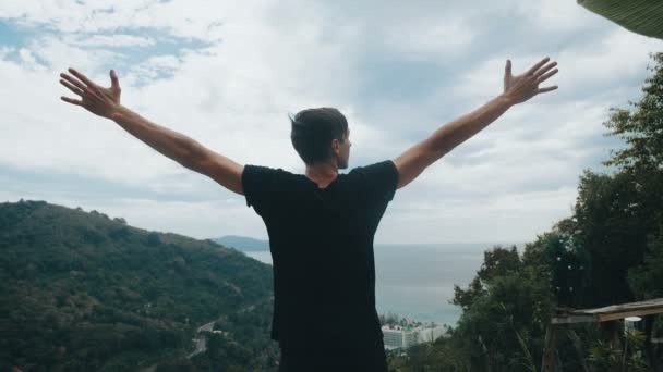 A fiatalember utazó magasra emeli a kezét a hegy tetején, a gyönyörű táj felett. - Felvétel, videó