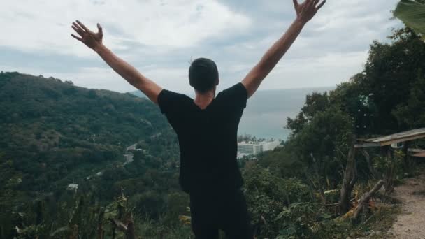 Jonge man reiziger steekt zijn handen hoog op de top van de berg boven prachtig landschap - Video