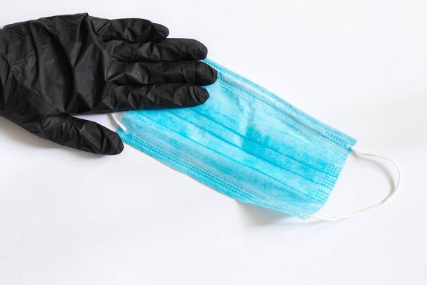 Medizinische blaue Schutzmaske und weibliche Hand in schwarzen Handschuhen auf weißem Hintergrund in Großaufnahme - Foto, Bild