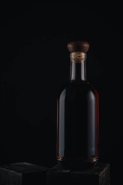 Glasflasche gefüllt mit Brandy oder Whisky auf schwarzem Hintergrund. Flasche alkoholisches Getränk auf Holztisch. - Foto, Bild