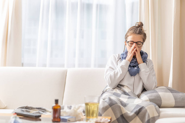 Girl sitting on a sofa and sneezing because of cold and fever. - Photo, Image