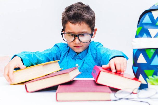 Netter Junge mit Brille sitzt an einem Schreibtisch mit Büchern - Foto, Bild