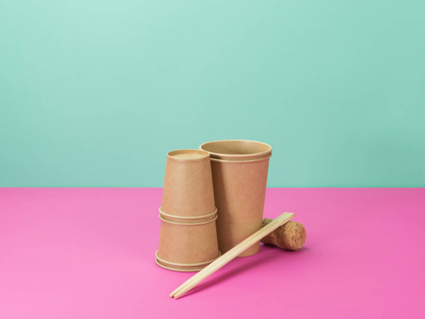 Vaisselle jetable de matériaux environnementaux sur fond rose et turquoise. . Tasses en papier, baguettes pour sushi et bouchon pour bouteilles
. - Photo, image