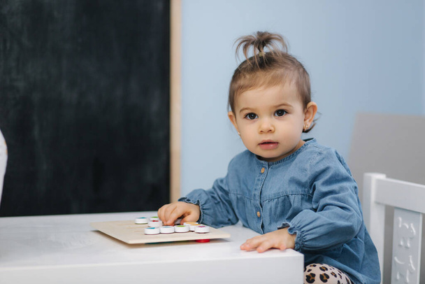 Kleine baby in de kleuterschool spelen. Een meisje in een blauw jeans shirt. Schattige kleine baby in de kinderkamer - Foto, afbeelding