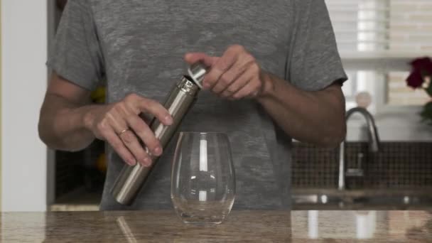 Young man in a gray T-shirt pours water into a glass from a thermos or plastic bottle in a beautiful fashionable kitchen. healthy lifestyle. Handsome man is thirsty. - Filmati, video