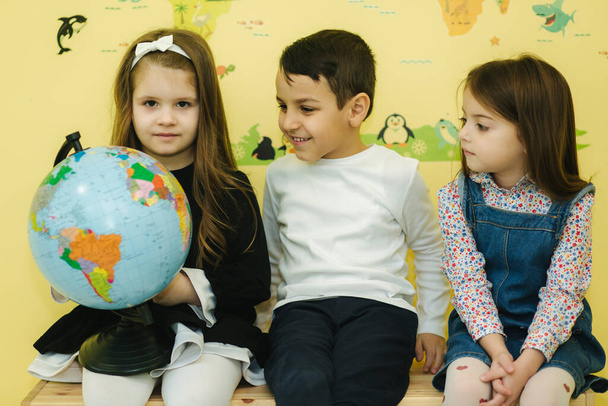 Мальчик с двумя девочками смотрит на земной шар и обыскивает разные континенты и страны
 - Фото, изображение