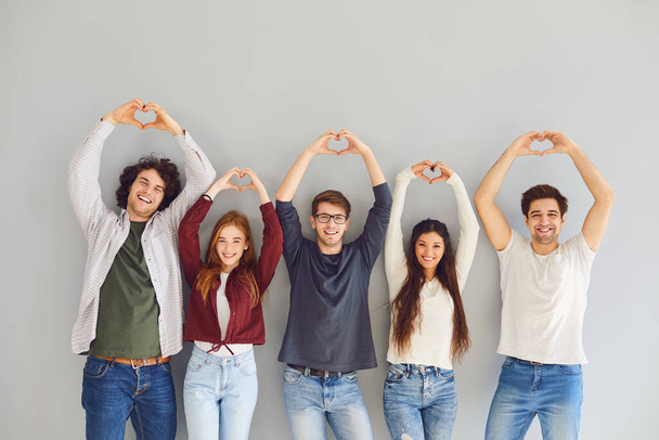 Group of friends making a heart with hands smiling while standing on gray background. - Fotografie, Obrázek