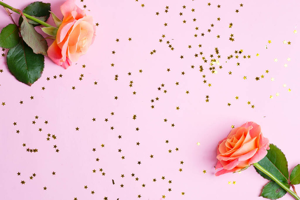 Esquina marco festivo de rosas frescas flores y carnaval decorativo estrellas confeti brillantes sobre un fondo rosa claro
. - Foto, imagen