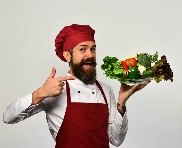 Chef points at bowl with vegetables. Cook with cheerful face - 写真・画像
