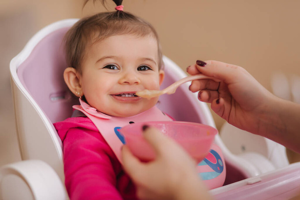Mała dziewczynka słodkie jedzą w wysokości krzesła. Portret małego uśmiechniętego dziecka w domu - Zdjęcie, obraz
