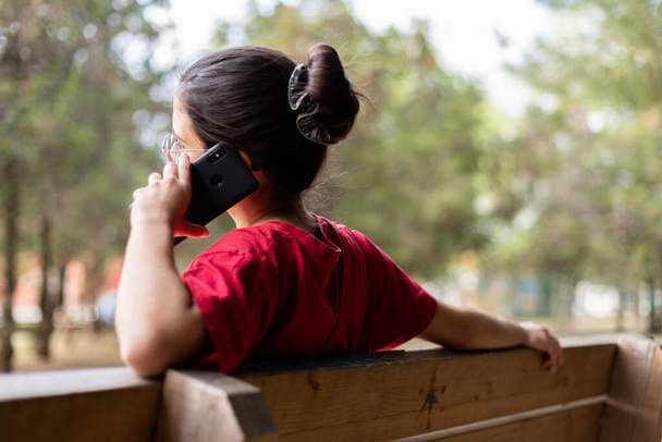 Nuori viehättävä nainen puhuu puhelimitse ja hymyilee puistossa, istu penkki
 - Valokuva, kuva