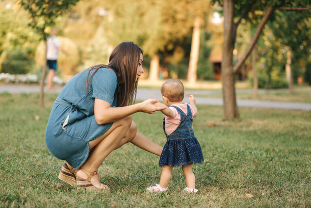 Πρώτο βήμα αξιολάτρευτου μικρού κοριτσιού στο καλοκαιρινό πάρκο. Η μαμά και η κόρη περπατούν - Φωτογραφία, εικόνα