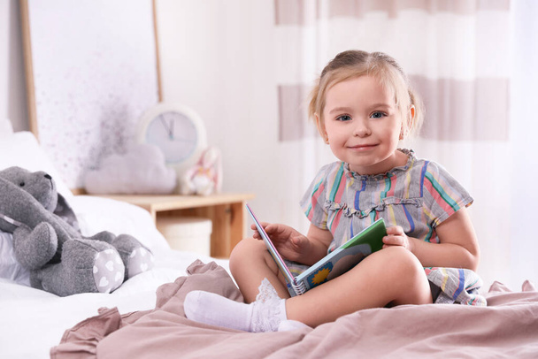 Cute little girl with book on bed at home - Foto, imagen