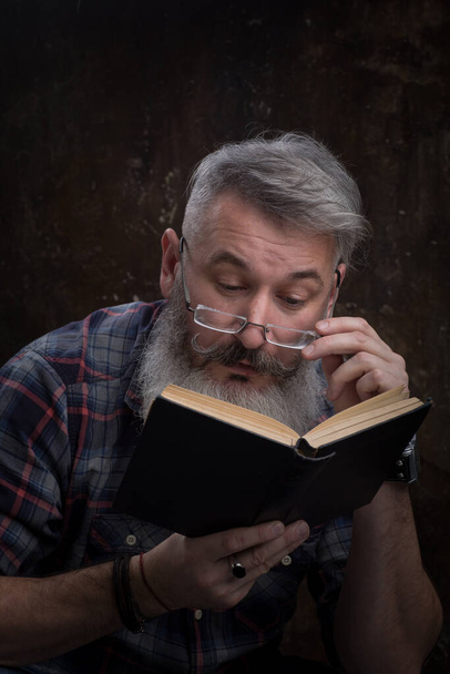 Portrait d'un barbu aux cheveux gris avec des lunettes lisant un livre, sur la couverture une inscription russe M. Gorky, mise au point sélective
 - Photo, image