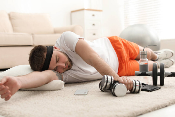 Lazy young man with sport equipment sleeping on floor at home - Photo, Image