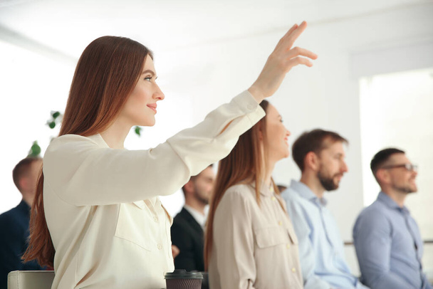 Young woman raising hand to ask question at business training indoors - Photo, image