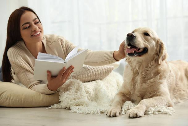 Young woman with book and her Golden Retriever at home. Adorable pet - Φωτογραφία, εικόνα