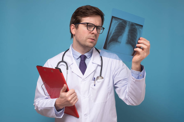 Мужчина врач, проверяющий рентгеновское изображение легких, фокусируется на рентгеновском снимке, подозревающем пневмонию.
 - Фото, изображение