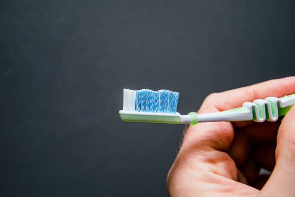 Primer plano mano masculina sosteniendo nuevo cepillo de dientes contra fondo gris
 - Foto, Imagen