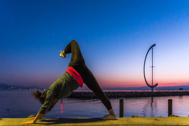 blonde woman doing yoga with her hands on the floor and her legs up in front of a lake in Lausanne in Switzerland during sunset - Valokuva, kuva