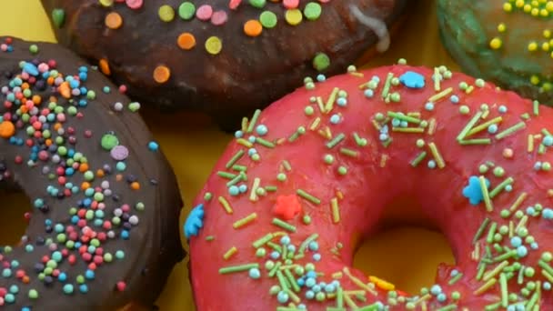 Amerikanische Donuts mit bunter Glasur und Puder. Drehen Sie auf einem gelben Hintergrund Nahaufnahme - Filmmaterial, Video