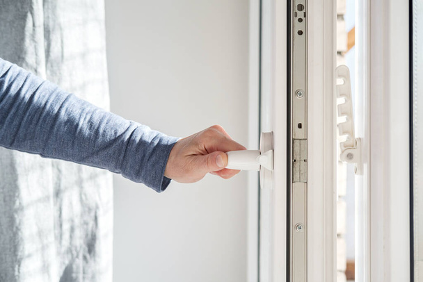 Hand opens a PVC window, holding the handle in a horizontal position, with a fixing device attached to the frame for ventilation. - Foto, afbeelding