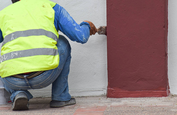 Primo piano: mano del pittore con pennello vernice marrone su muro di cemento
. - Foto, immagini