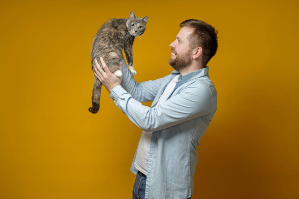 Joyful owner holds his adorable cat in hands, looks at her and smiles. Concept of love for pets. - Fotografie, Obrázek
