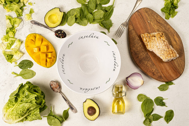 Белый глубокий салат миска и свежие ингредиенты для резкий гриль куриный салат с свежим манго, авокадо, шпинат и салат на светлом фоне, вид сверху
   - Фото, изображение