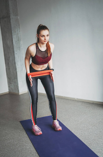 Çekici formalı genç bayan spor giyim fitness mankeni elastik bant ile çatı katı çalışma sınıfında esneme hareketleri yapıyor. - Fotoğraf, Görsel