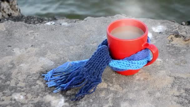 Red cup with hot coffee tea and steam, tied with blue knitted scarf - Footage, Video