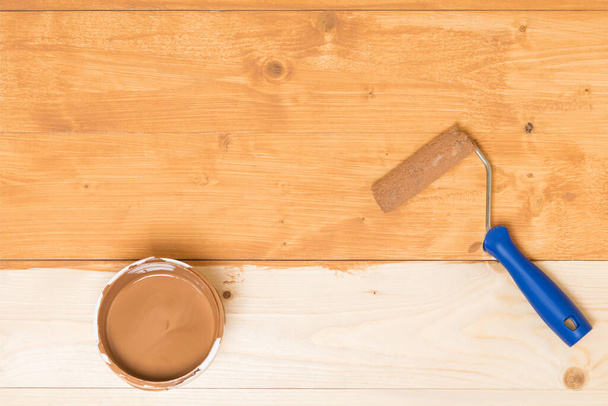 can of varnish and paint roller on a wooden floor half painted with dark varnish - 写真・画像