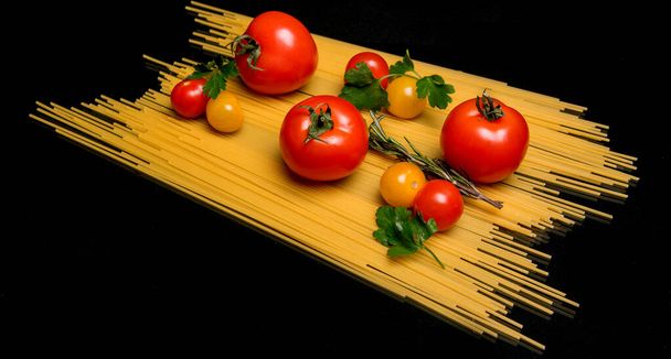 Tomatoes, ripe, dill, mint, rosemary on spaghetti, pasta on a black background - Photo, Image