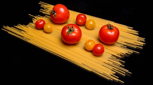 Tomatoes on spaghetti, pasta on a black background - Photo, Image