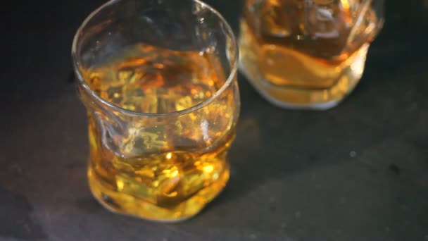 Two glasses of whiskey with ice on a black table. Ice falls in a glass. - Filmmaterial, Video