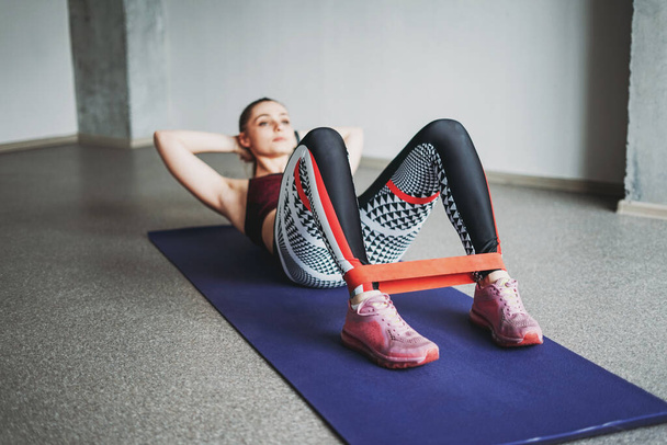 Aantrekkelijke pasvorm jonge vrouw sport dragen fitness meisje model doen stretching met elastische band doen sit-ups in loft studio workout klasse - Foto, afbeelding