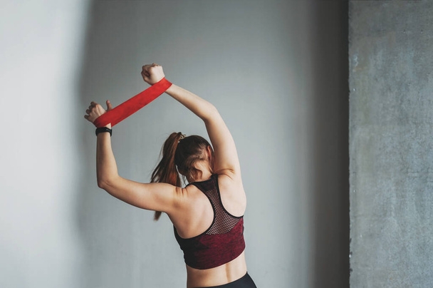 Çekici formalı genç bayan spor giyim fitness mankeni elastik bant ile çatı katı çalışma sınıfında esneme hareketleri yapıyor. - Fotoğraf, Görsel
