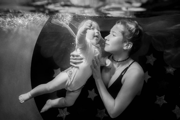 Monochrome film portret van moeder met baby dochter onder water in het zwembad aan de hemel, sterren en de maan achtergrond. Sport, familie, liefde en sprookjesconcept - Foto, afbeelding
