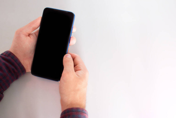 holding a mobile phone with a blank black screen. reads from a smartphone on a light background with place for text mockup - Photo, Image