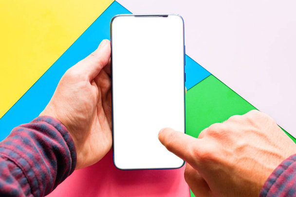 holding a smartphone with a blank white screen and clicks on the touch screen of the phone on a colored background - Foto, Imagem