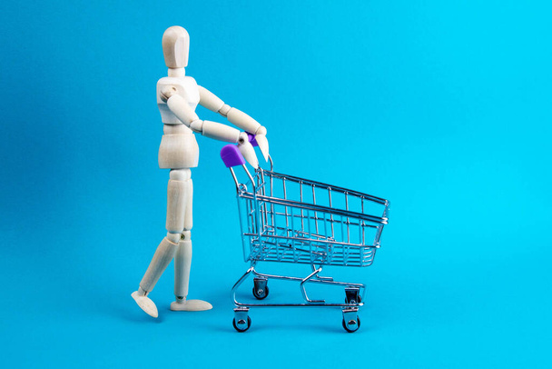 Shopping concept. Wooden doll and metal shopping cart. - Photo, Image